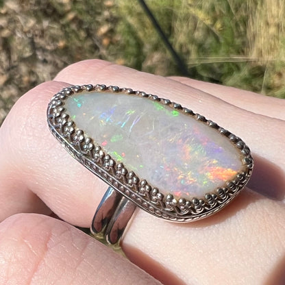 Angled macro view of an Australian opal ring in sterling silver, worn on a hand in natural sunlight.  The opal has soft multicolor play of color.