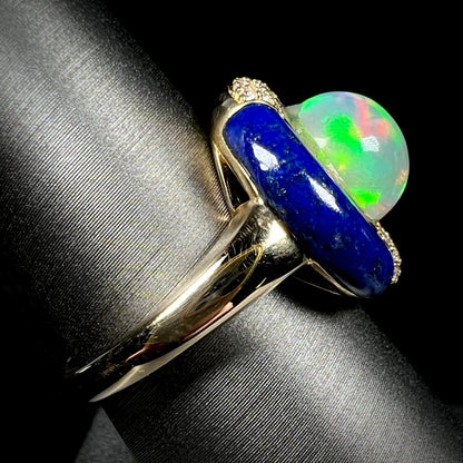 Side close-up view of a solid 14k yellow gold Ethiopian opal and lapis lazuli women's ring on a display.  The ring's shank is in clear focus.