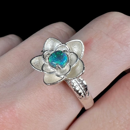 Angled close-up of solid black opal flower ring made from sterling silver, worn on finger