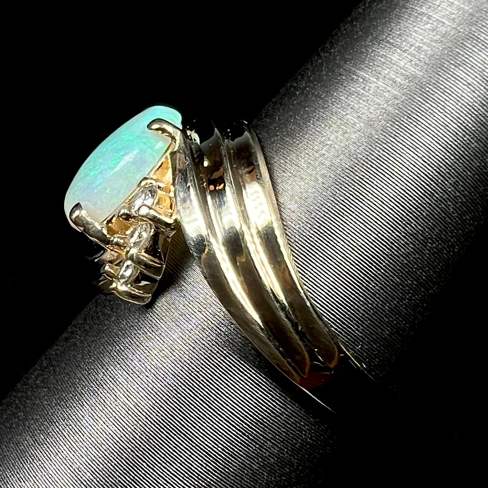 Side view of solid 14k yellow gold opal and diamond ring on ring display, focused on ring's shank