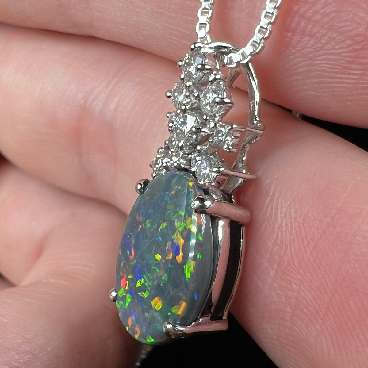 Side macro view of natural black opal pendant with solid composition and N3 body tone, held in hand.