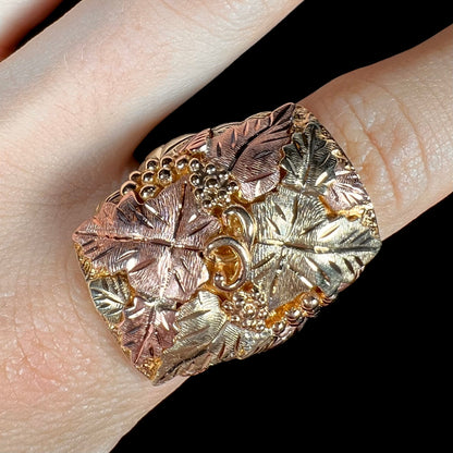 A men's solid gold ring.  The ring is Black Hills gold featuring a grapevine and leaf motif with rose and green gold designs.