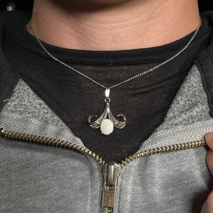 A Sorrento brand sterling silver Australian white opal pendant worn around a neck against a dark shirt.