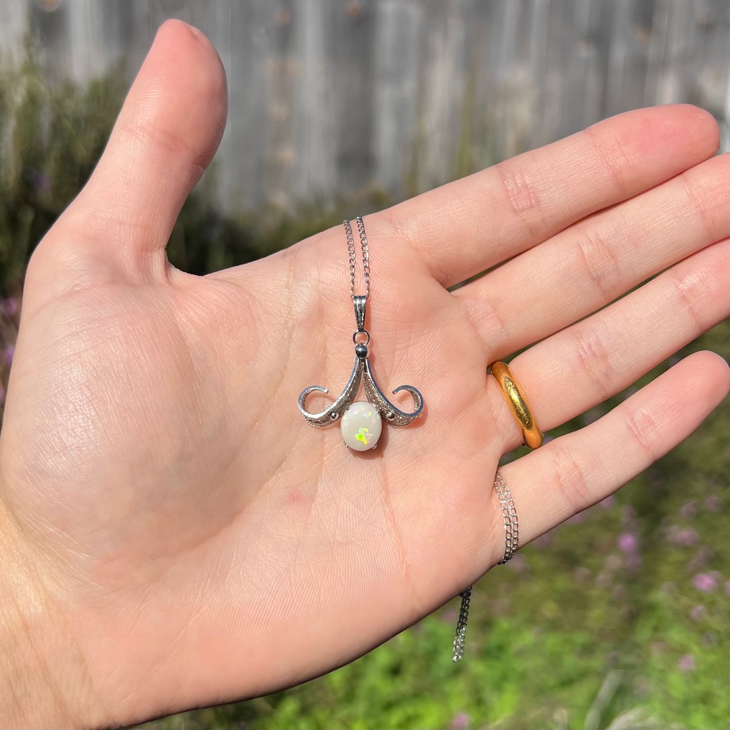 A Sorrento brand sterling silver Australian white opal pendant shown in a hand in the outdoor sunlight.