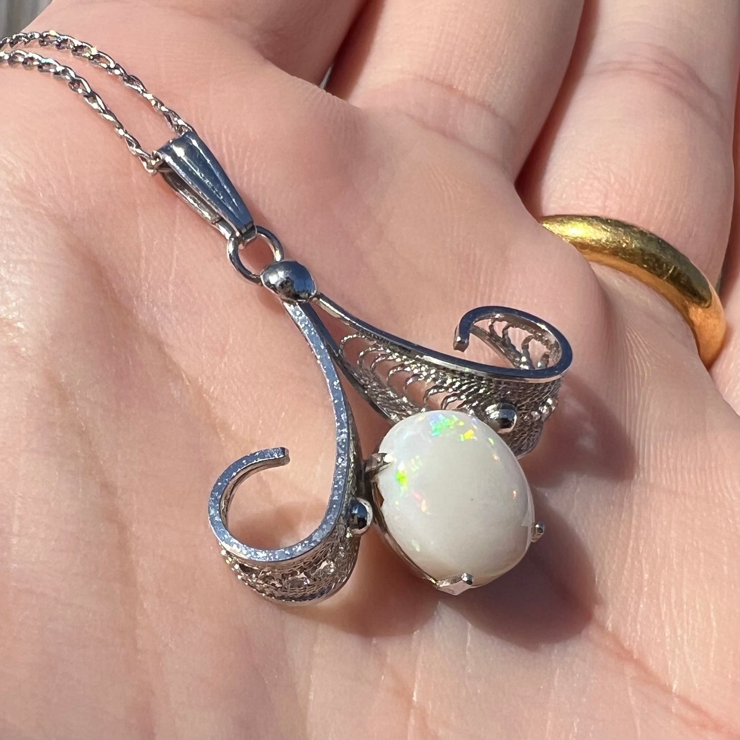 A Sorrento brand sterling silver Australian white opal pendant shown from an angle in a hand in sunlight.