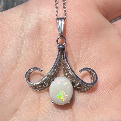 Close-up of a Sorrento brand sterling silver Australian white opal pendant in a hand, flashing green in the sunlight.