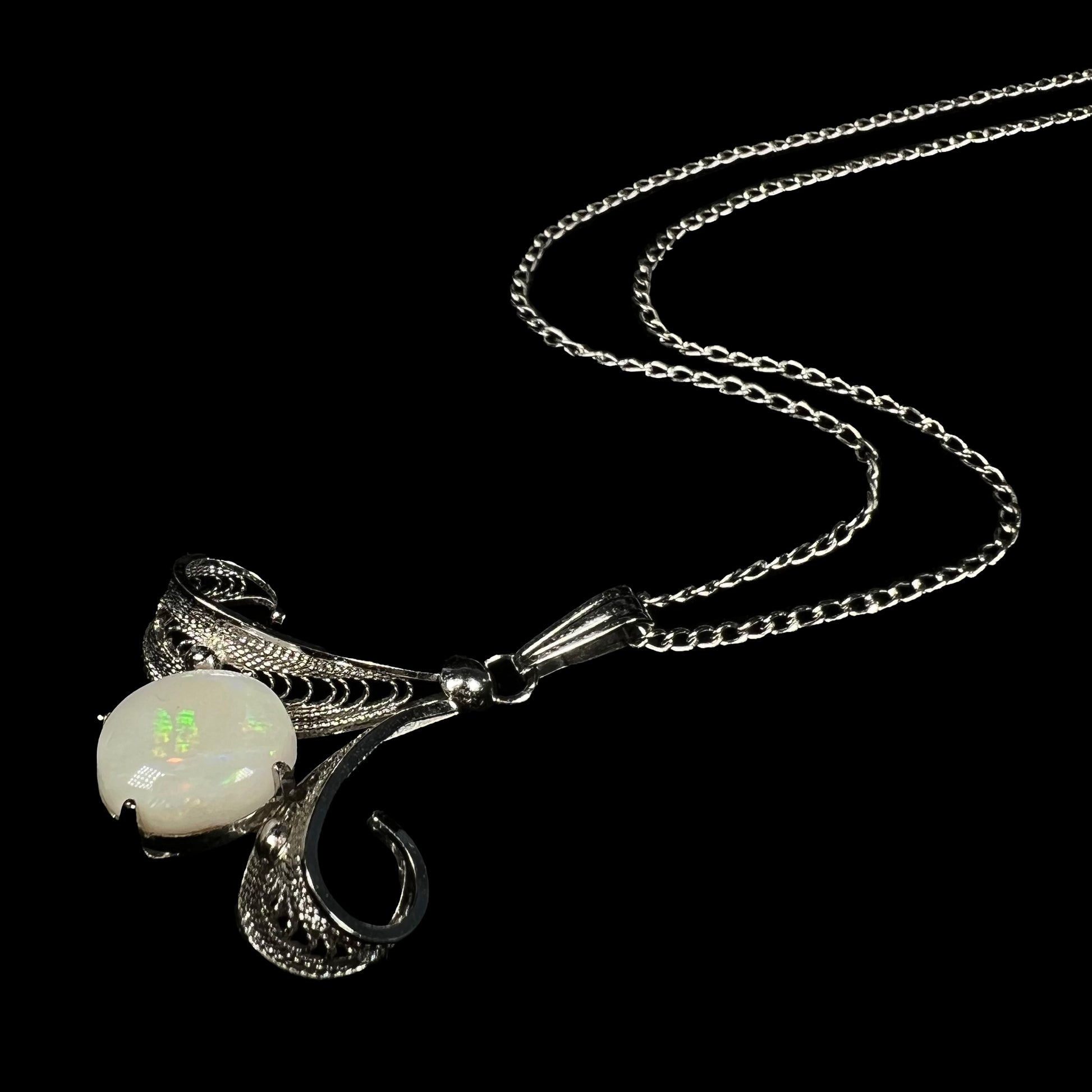 A Sorrento brand sterling silver Australian white opal pendant shown at an angle laying on a black backdrop.