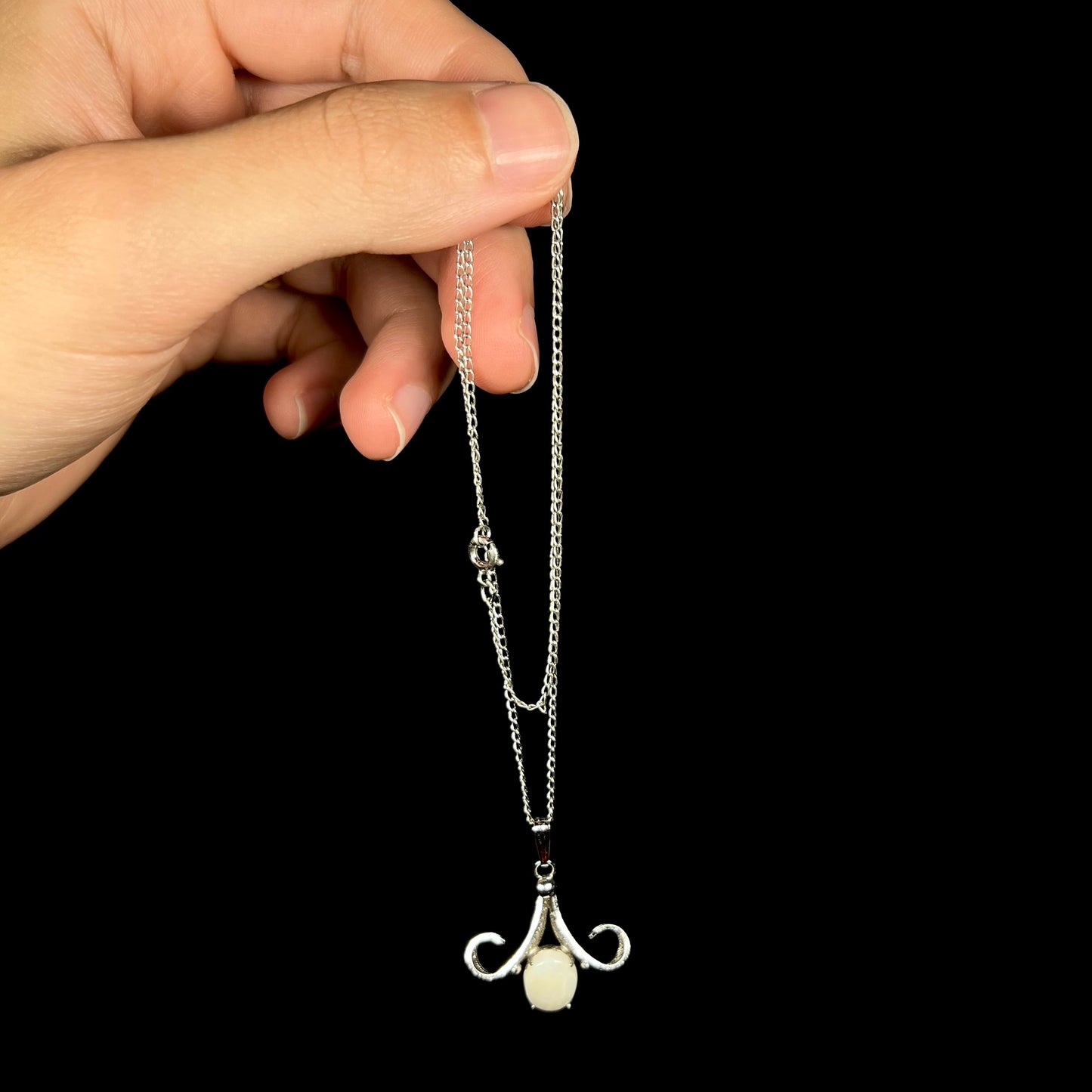 A Sorrento brand sterling silver Australian white opal pendant, dangled by a hand from its chain.