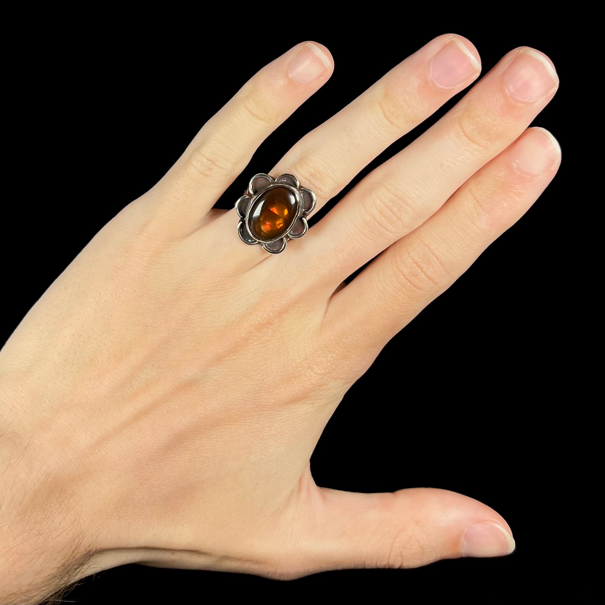 Fire agate ring worn on hand, glowing with orange iridescence.