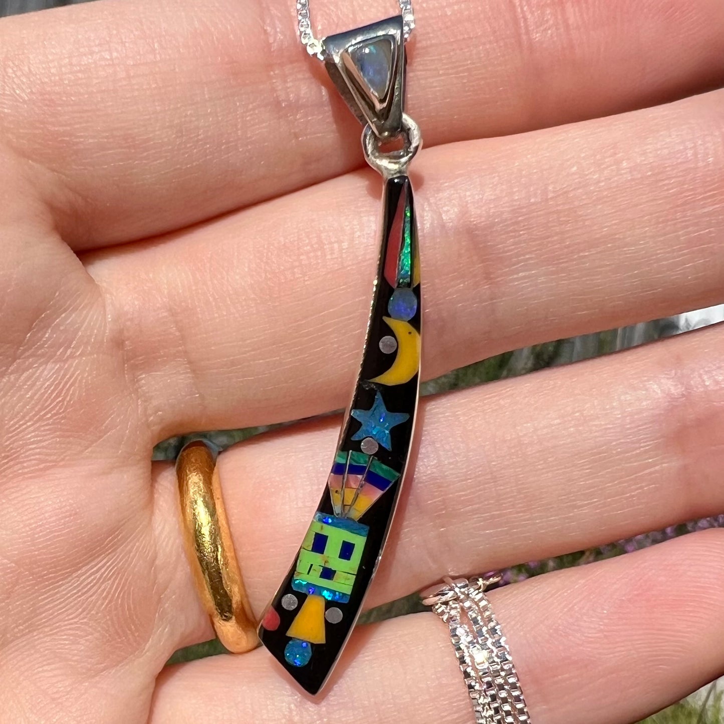 Close-up of Southwest opal inlay pendant with space motif shown in hand under natural sunlight.
