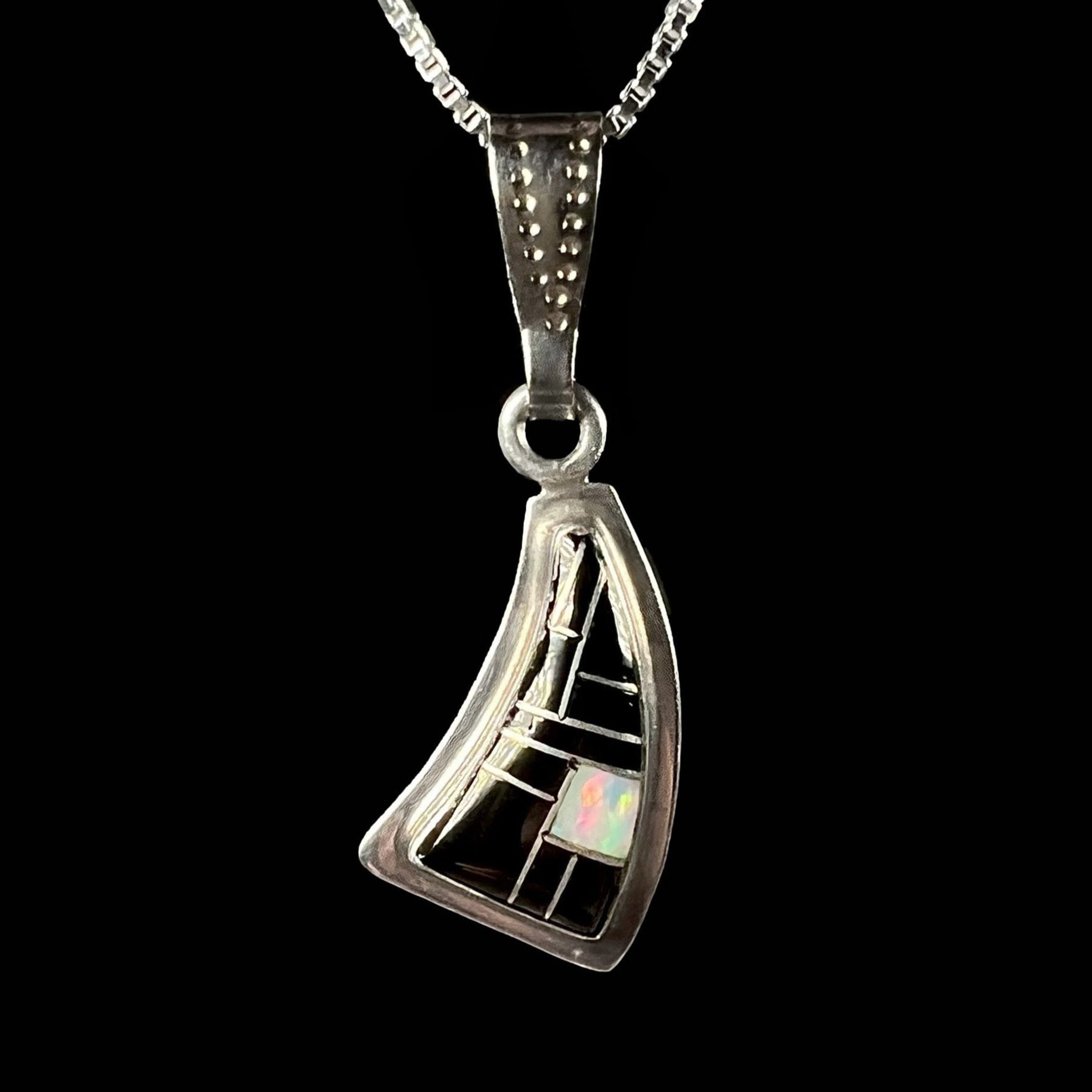 Curved, Southwestern-style silver necklace inlaid with opal and black onyx, set against a black background.