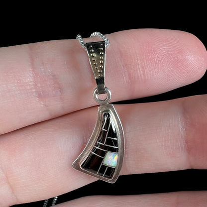 Close-up of Southwest-style silver opal and onyx necklace held on fingers, macro view against a black background.