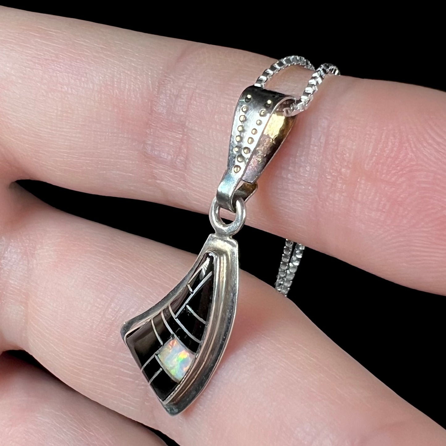 Opposite side angle of Southwest-style silver opal and onyx necklace held on fingers against a black background.