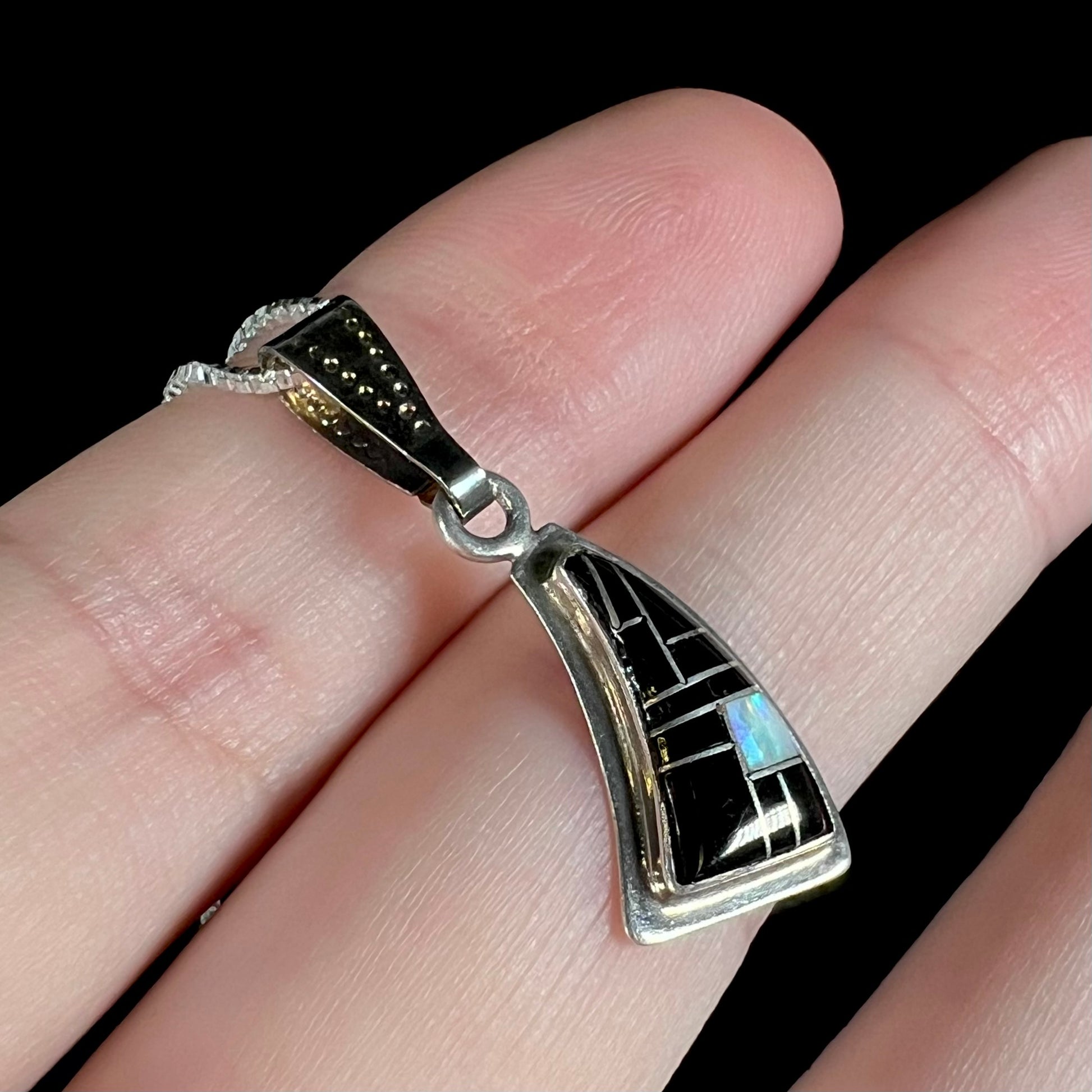 Side angle of Southwest-style silver opal and onyx necklace held on fingers against a black background.