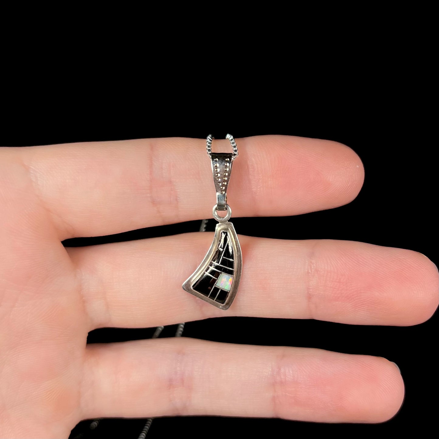 Southwest-style silver opal and onyx necklace held on fingers, viewed straight-on against a black background.