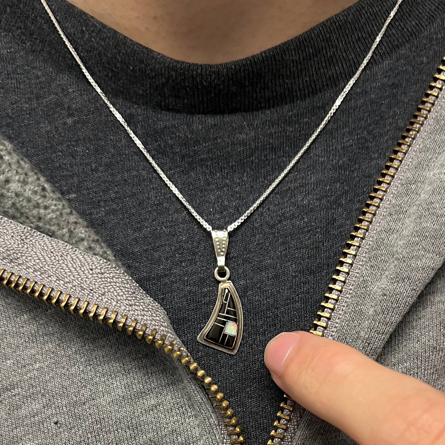 Southwest-style silver opal and onyx necklace worn on a neck, seen against a black shirt and open sweatshirt.