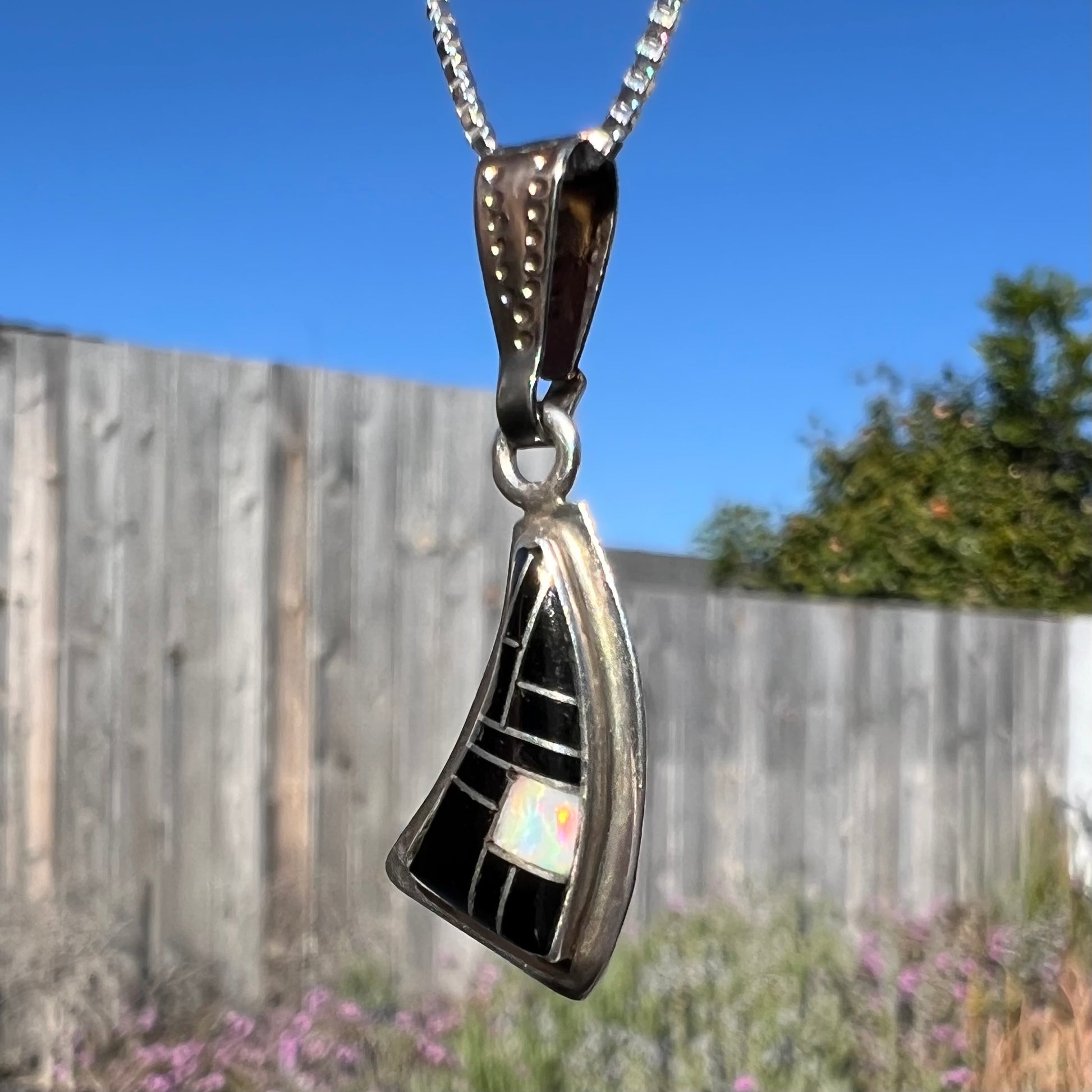 Angled side view of Southwest-style silver opal and onyx necklace outside, showing opal color play in natural light.