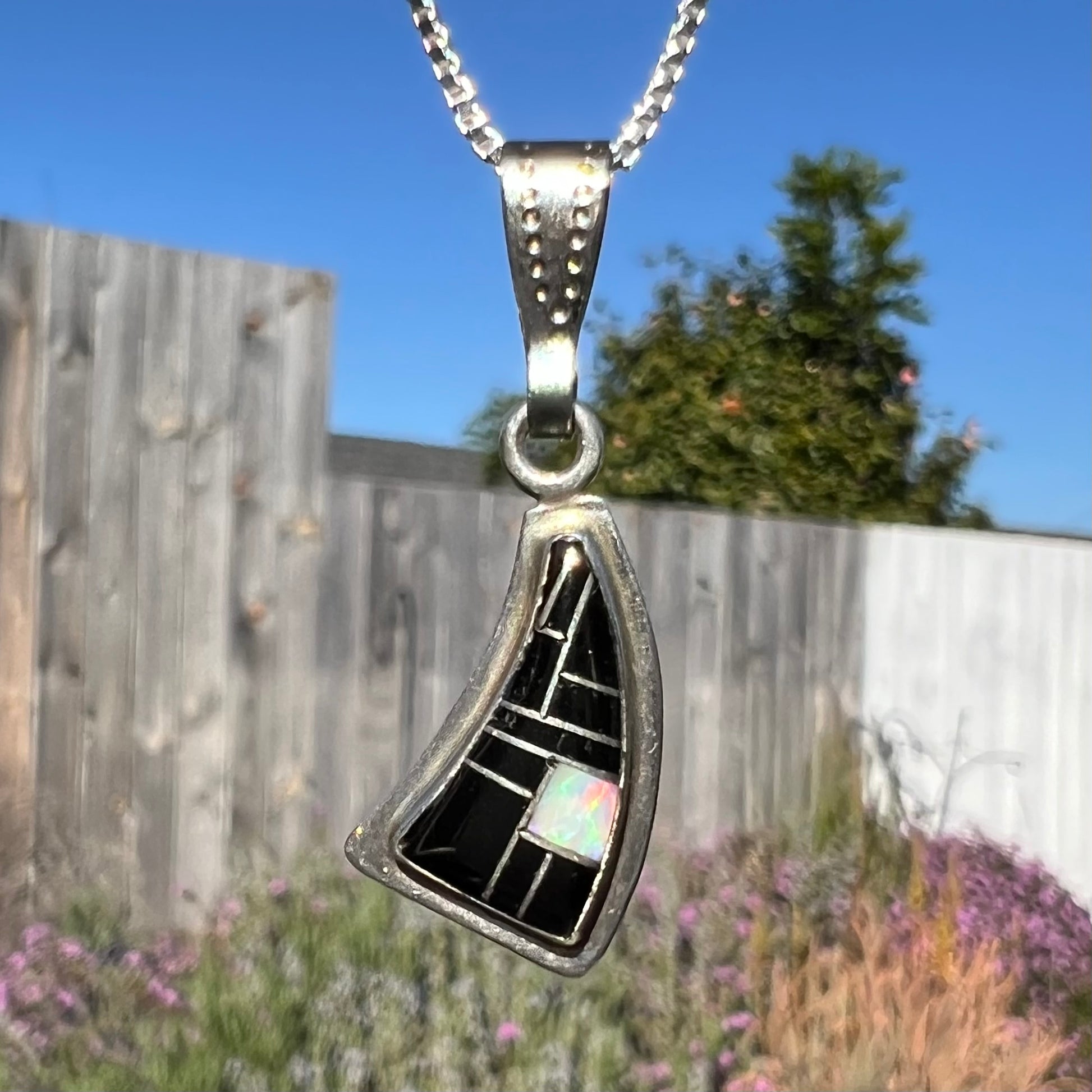 Close-up macro view of Southwest-style silver opal and onyx inlay necklace outside, showing opal color play in natural light.