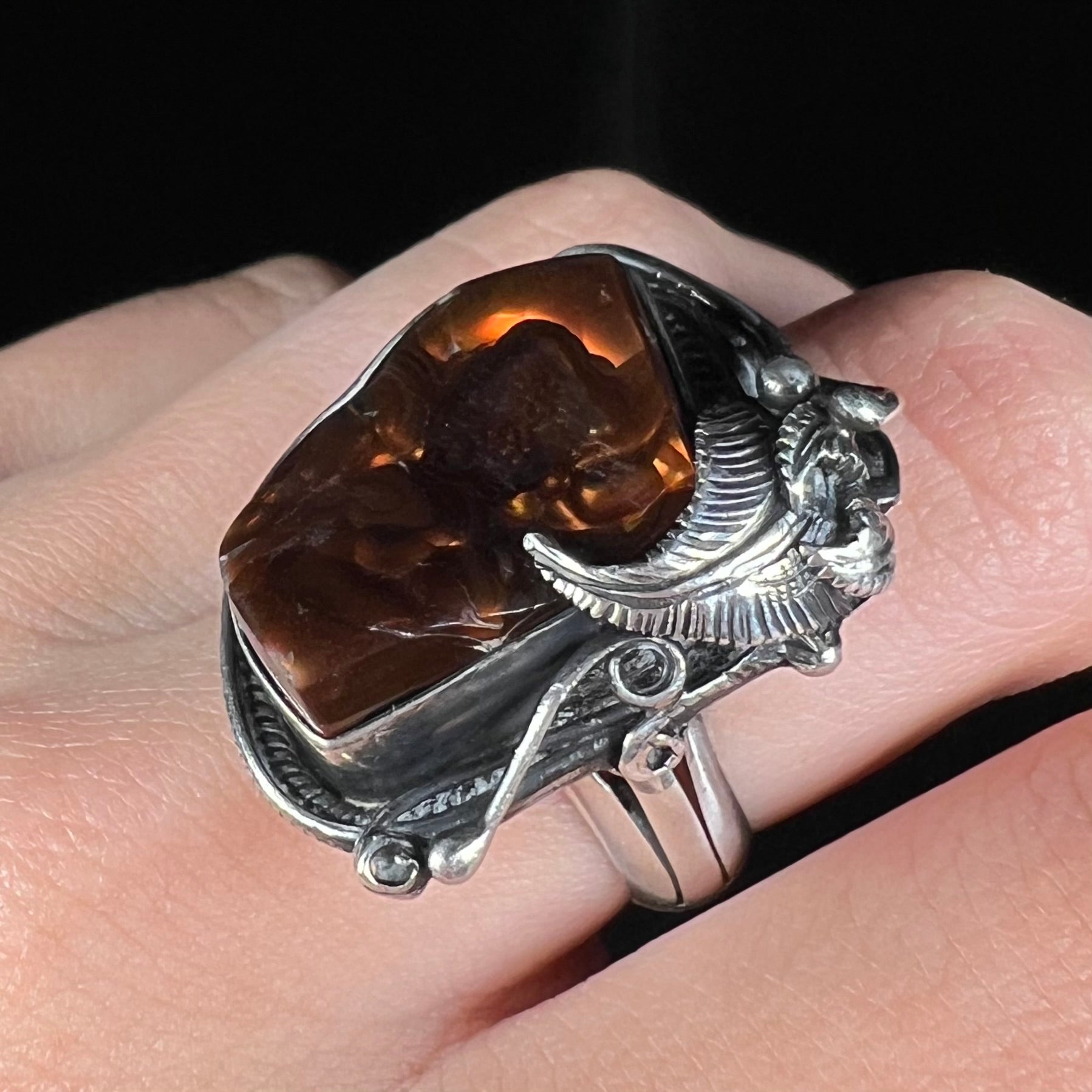 A men's silver, Southwest-style fire agate ring worn on a finger and shown at an angle close-up.