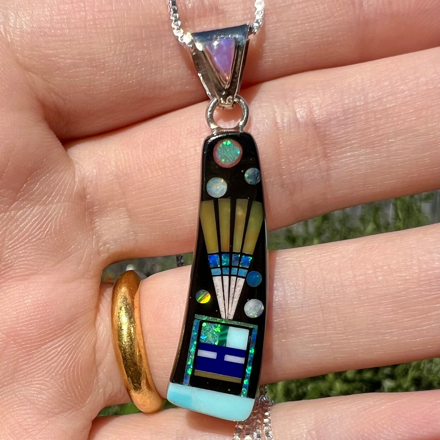 Close-up of Southwest-style opal and onyx inlay pendant with kachina design shown held in hand in natural light.
