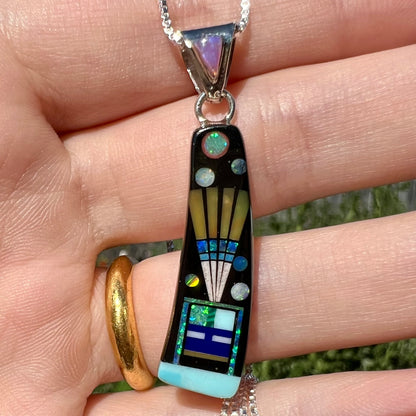 Close-up of Southwest-style opal and onyx inlay pendant with kachina design shown held in hand in natural light.