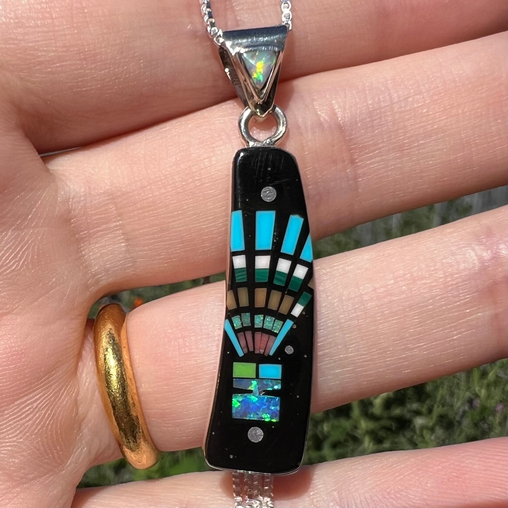 Close-up of sterling silver Southwest-style lab-created opal and onyx inlay pendant, held in hand under natural light.
