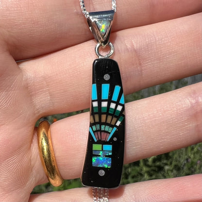 Close-up of sterling silver Southwest-style lab-created opal and onyx inlay pendant, held in hand under natural light.