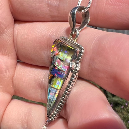 A Southwest-style opal mosaic triplet pendant in sterling silver shown from the side view in sunlight, held in hand.  The large bail can be seen with a box chain.