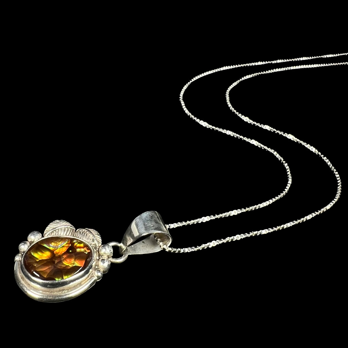 Unisex Soutwest-style sterling silver fire agate necklace shown laying on black background, the pendant's chain flowing into the distance.