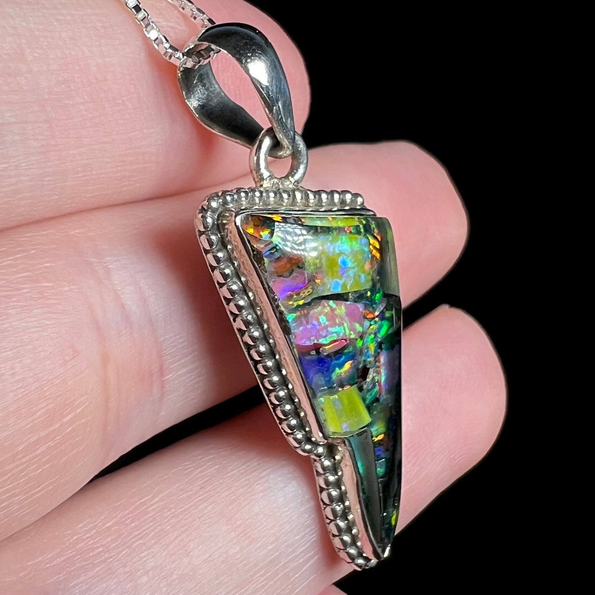 Sterling silver mosaic opal pendant with Southwest-style beading along its sides, shown close-up from side view in hand.