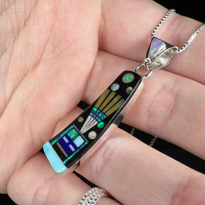 Space-inspired silver multi-stone inlay pendant with kachina design shown close-up from ange in hand under studio light.