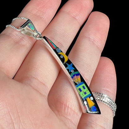 Space-themed multi-stone inlay pendant shown from angle in hand against black background.