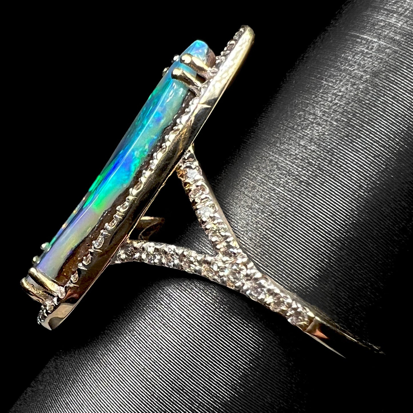 Side view of yellow gold boulder opal  ring with a pave-set diamond split shank, shown on a ring display against a black backdrop.