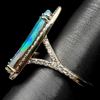 Side view of yellow gold boulder opal  ring with a pave-set diamond split shank, shown on a ring display against a black backdrop.