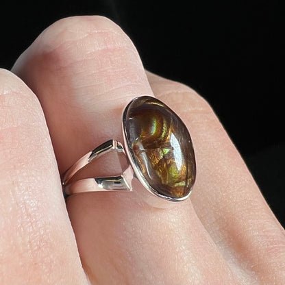 Angled close-up of a sterling silver Mexican fire agate ring with a split shank on a finger.