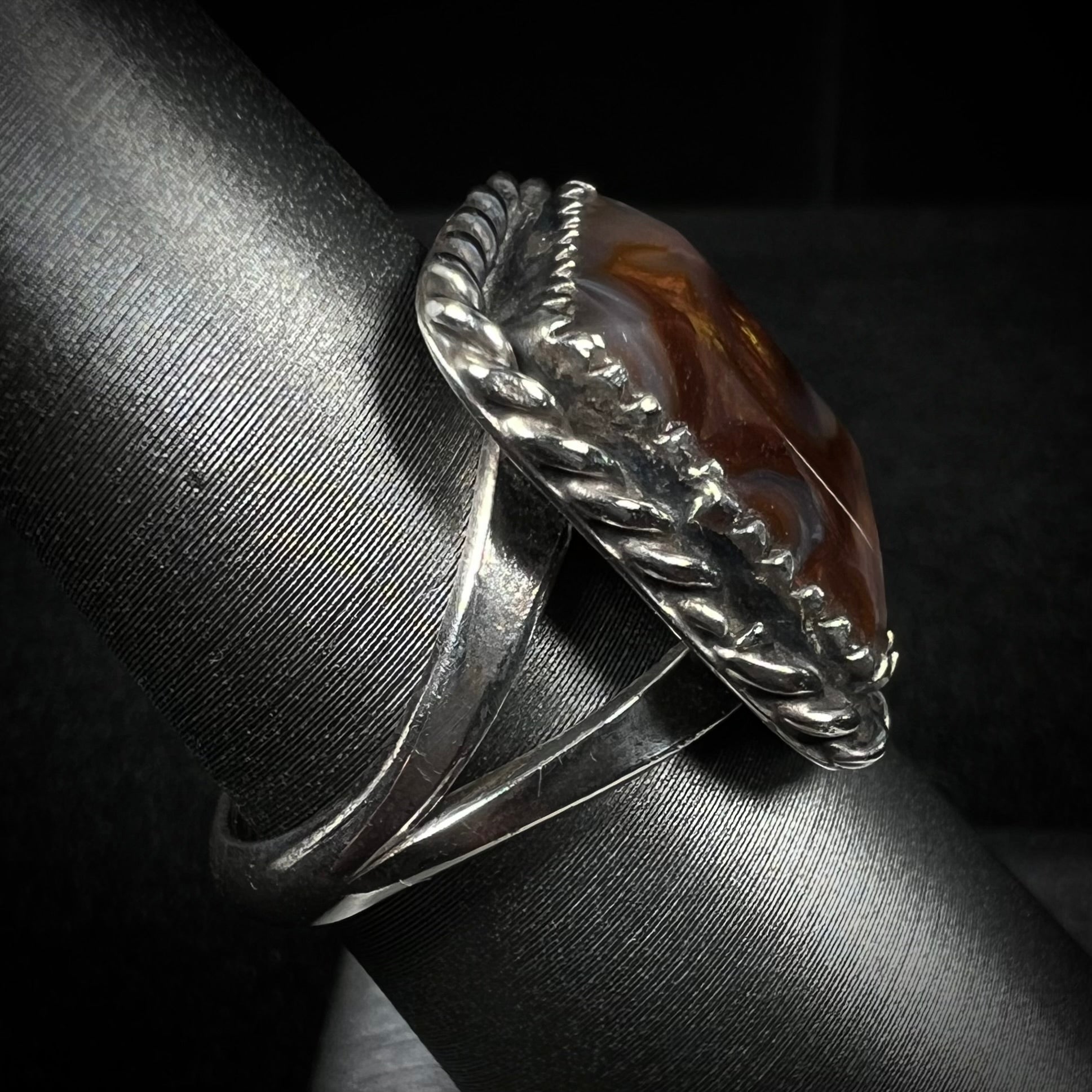 Side view of split shank fire agate ring with rope design against dark backdrop.