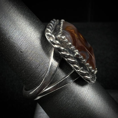 Side view of split shank fire agate ring with rope design against dark backdrop.