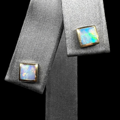 Pair of square shaped opal stud earrings in 14k gold on earring display