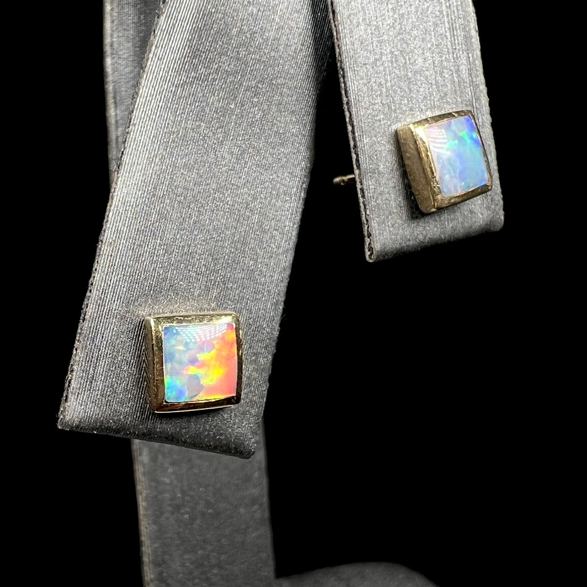 Square cut opal stud earrings on earring display.  One opal has red flash.