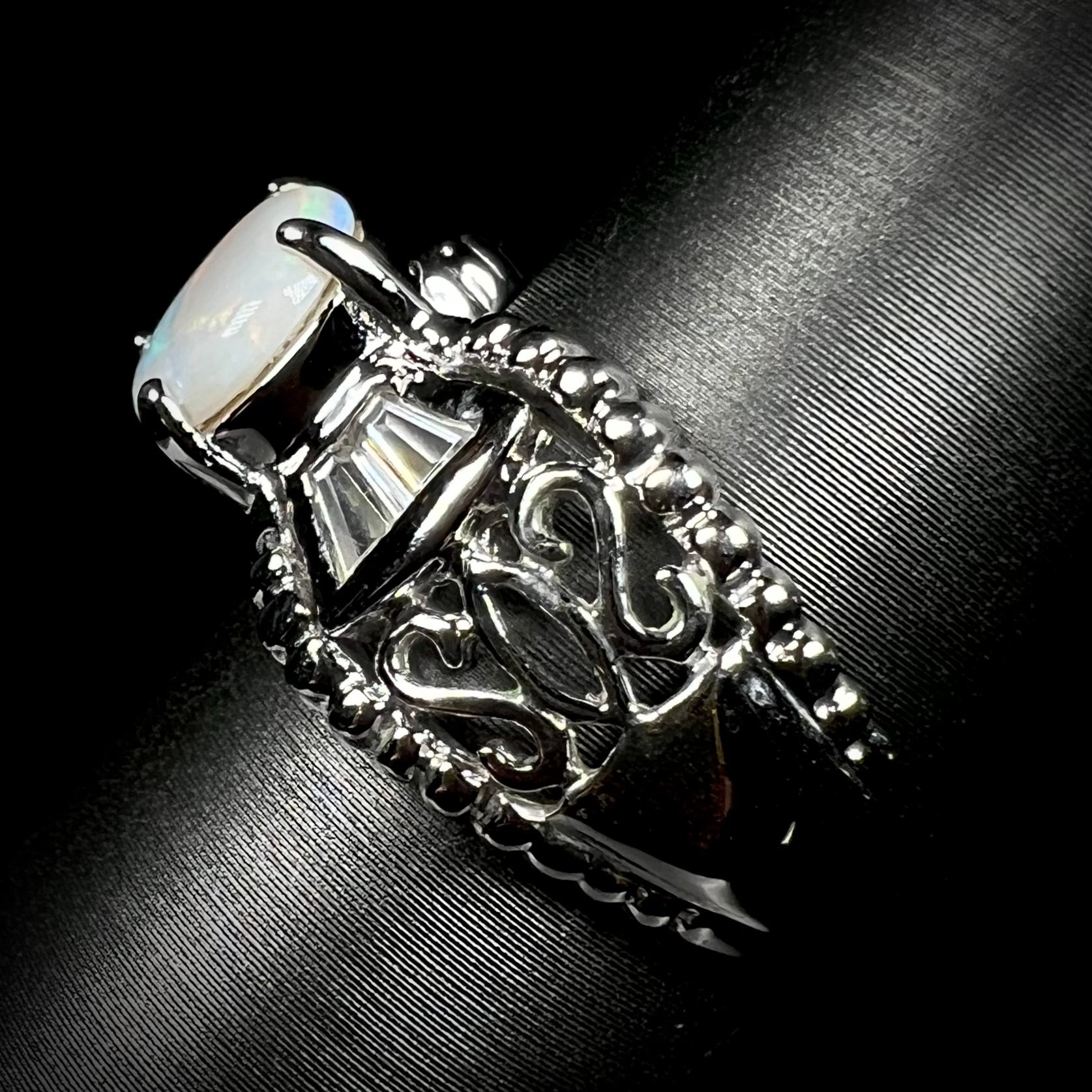 Side view of a a round Australian white opal and CZ ring in white base metal, focusing on the ring's shank.