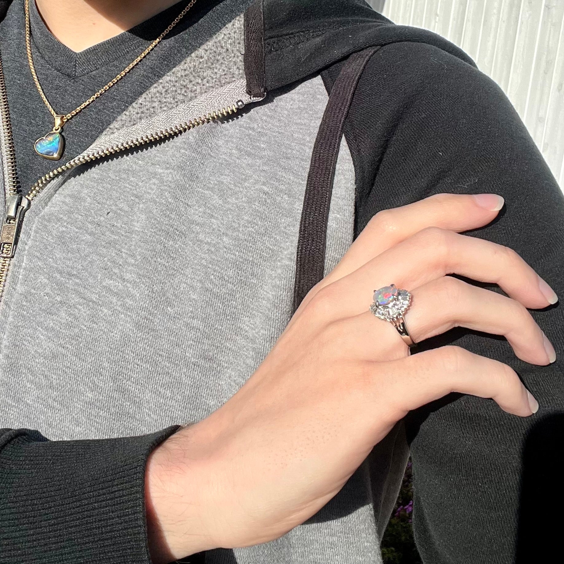 A model showcases a semi-black opal and diamond platinum statement ring on his hand in the sunlight.