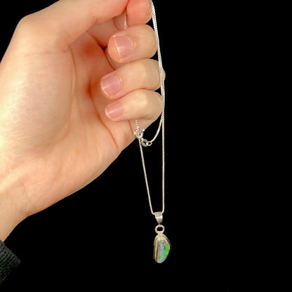 Hand dangling sterling silver Australian black opal necklace from its chain.