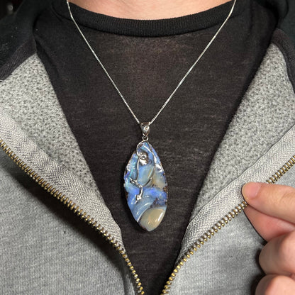 A large, blue Australian boulder opal necklace in sterling silver, worn around a neck against a dark shirt.