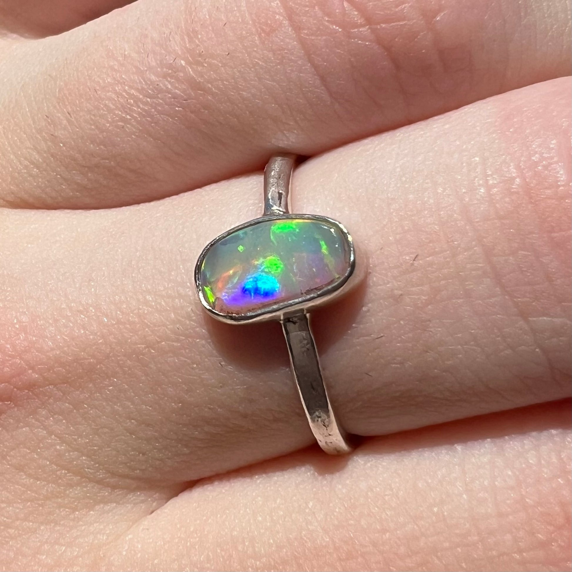Angled close-up of a sterling silver Australian crystal opal solitaire ring in natural outdoor light, worn on a finger.