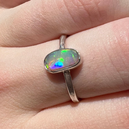 Angled close-up of a sterling silver Australian crystal opal solitaire ring in natural outdoor light, worn on a finger.