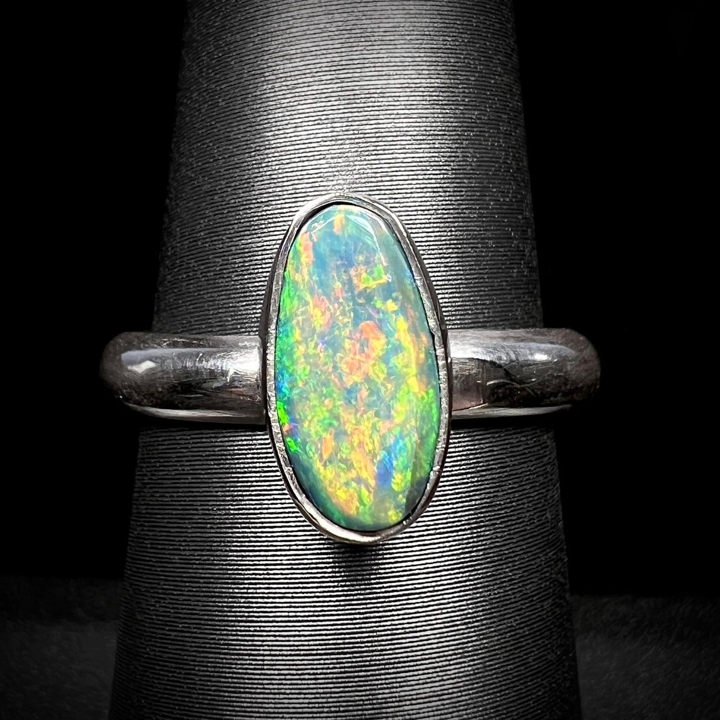 Close-up macro view of a sterling silver Lightning Ridge, Australian dark opal solitaire ring with muted green and orange fire, shown on a ring display.