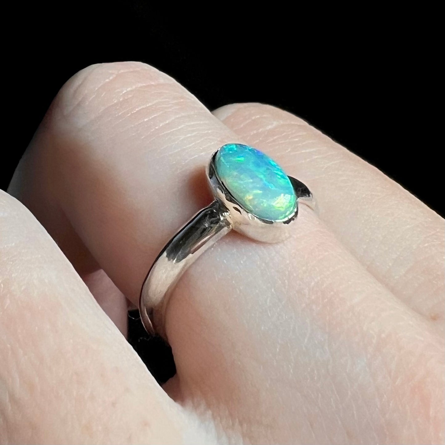 Macro view of a sterling silver Australian opal women's ring worn on a finger and shown from an angle.