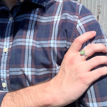 Hand wearing a sterling silver Australian opal ring in sunlight as it rests on the person's opposing shoulder.