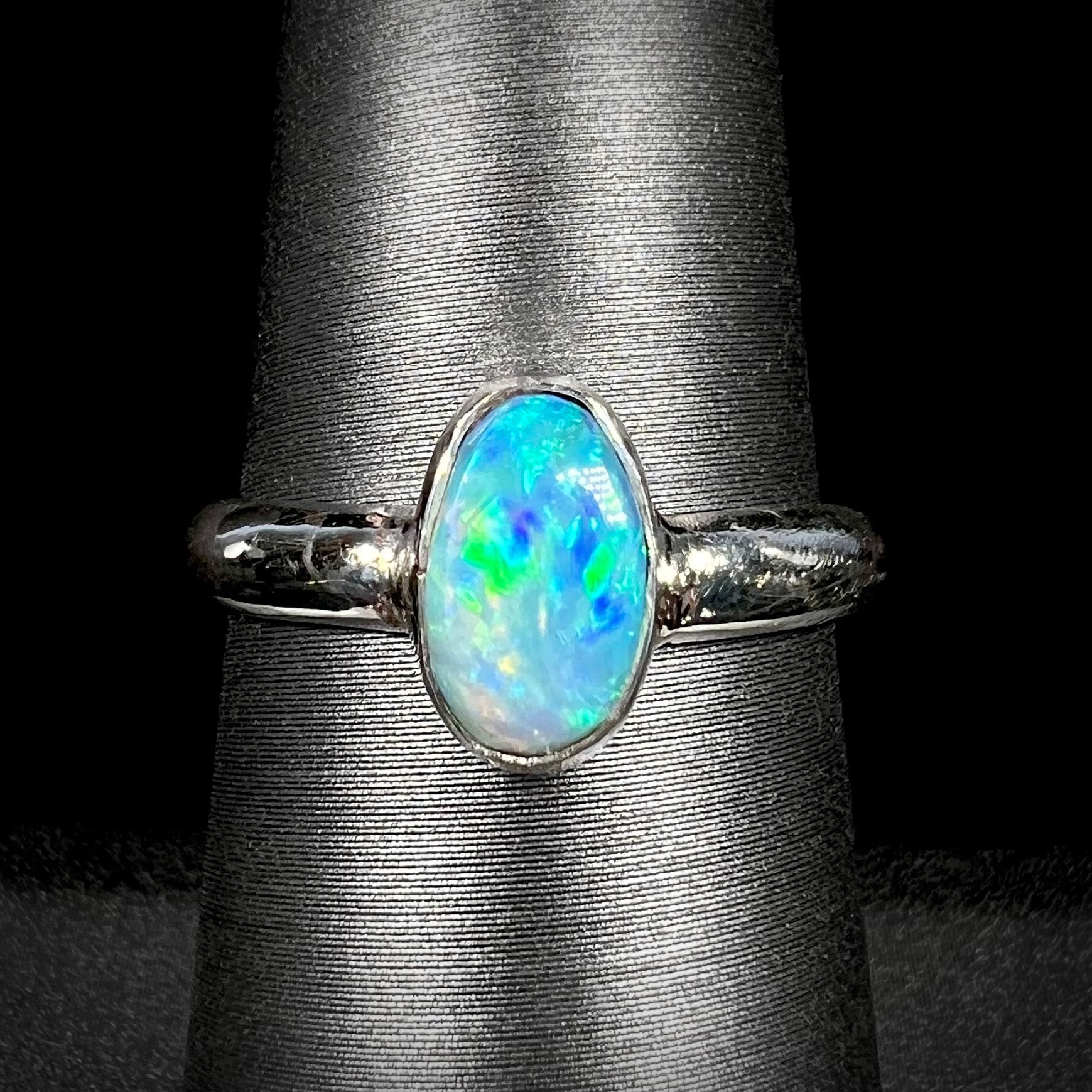 A women's pure silver Australian opal solitaire ring with blue and green colors shown close-up on a ring display against a black background.