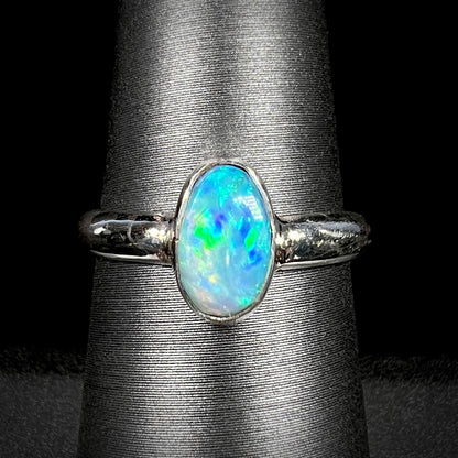 A women's pure silver Australian opal solitaire ring with blue and green colors shown close-up on a ring display against a black background.